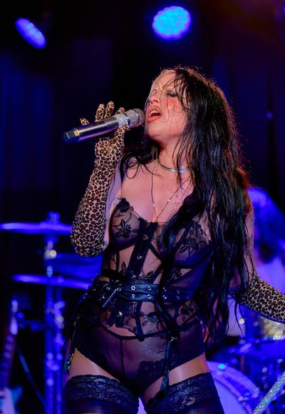Kelsy Karter sings into a jeweled microphone under blue stage lights, wearing leopard-print gloves.