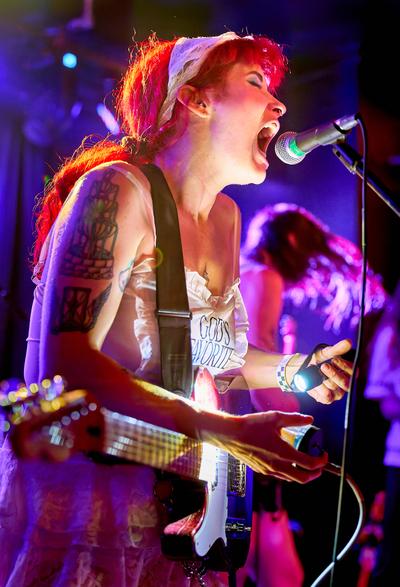 A member of Latter sings into a microphone while playing bass under red and purple stage lights at Altar.
